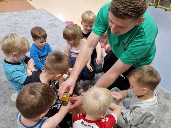 Trener przybija nagradzające pieczątki dzieciom zebranym w kręgu po treningu Sportuś
